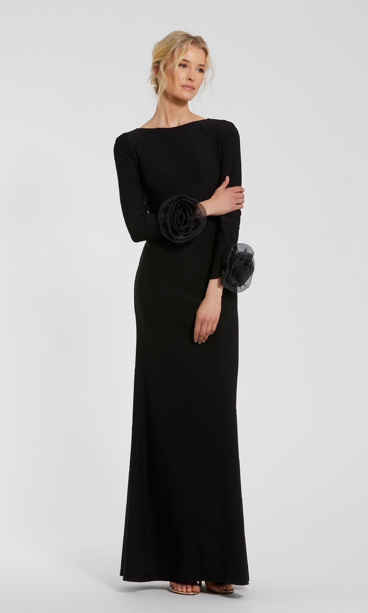 A woman stands against a plain light gray background, wearing the Mac Duggal 49949 long sleeve long formal dress with floral sleeve accents.